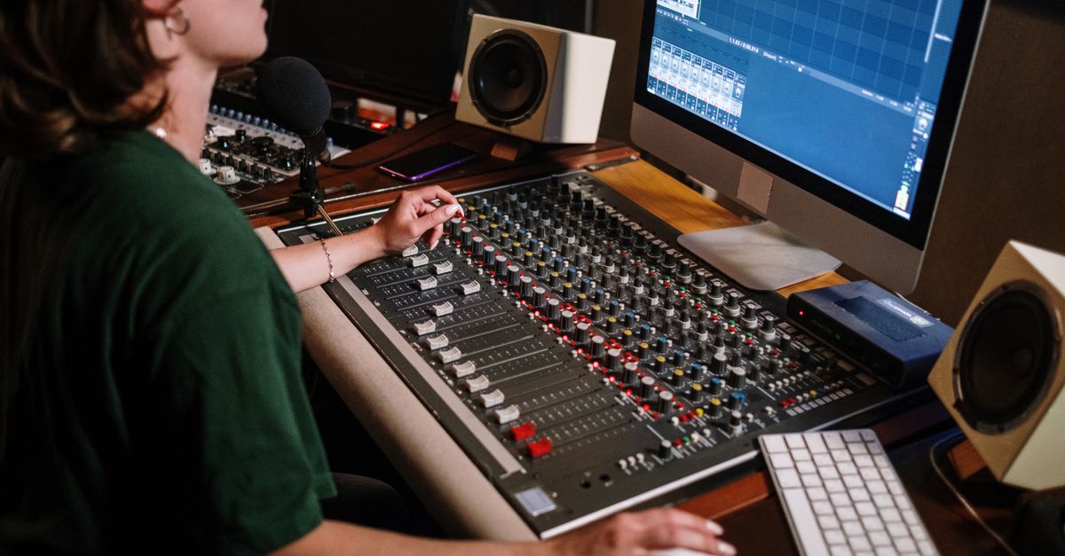 A sound engineer adjusting audio levels at a mixer desk in a recording studio with high-tech equipment.