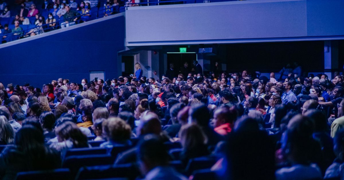 A crowded conference hall with diverse audience attentively listening to a speaker.