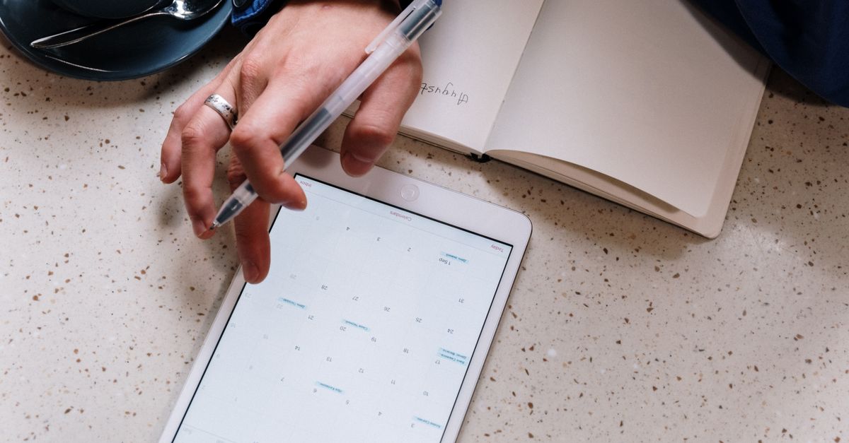 Person using a tablet for planning with an open notebook and coffee. Ideal for tech and productivity visuals.