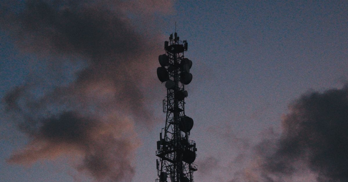 Silhouette of a telecommunications tower against a vibrant twilight sky with clouds.