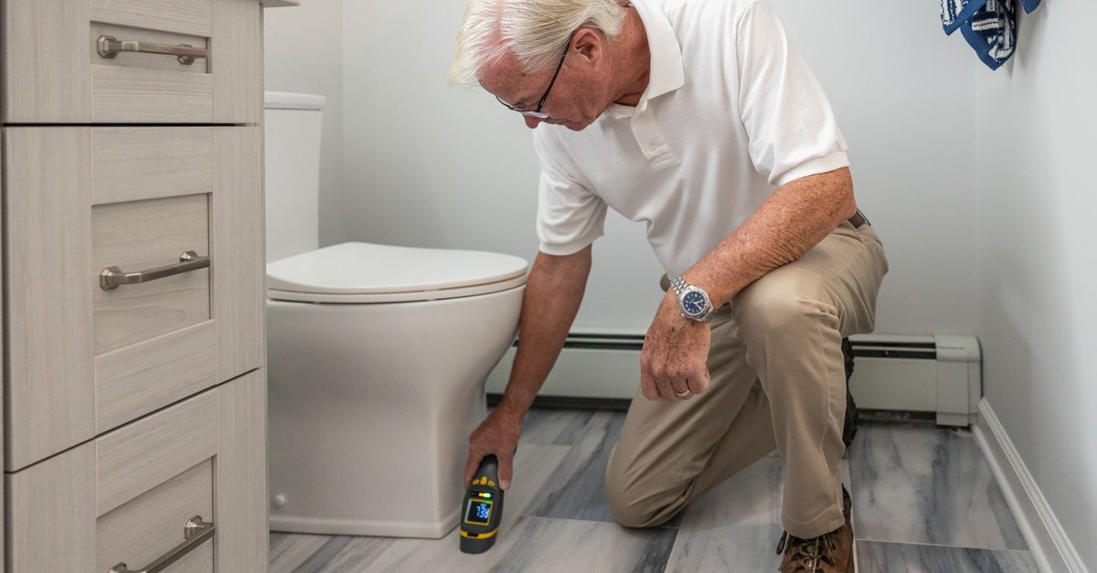 A senior man using a device to inspect a bathroom for maintenance or repair.