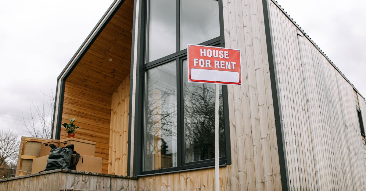 Low-angle view of a modern wooden house with a 'House for Rent' sign, showcasing contemporary architecture.