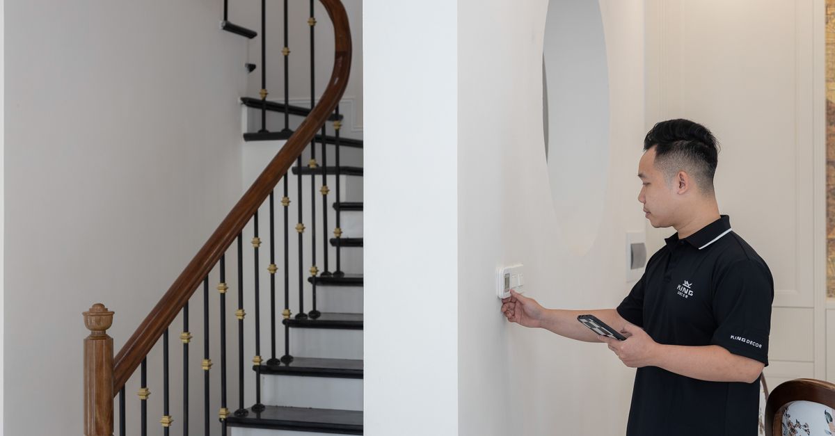 Man adjusting thermostat in stylish home with elegant staircase.