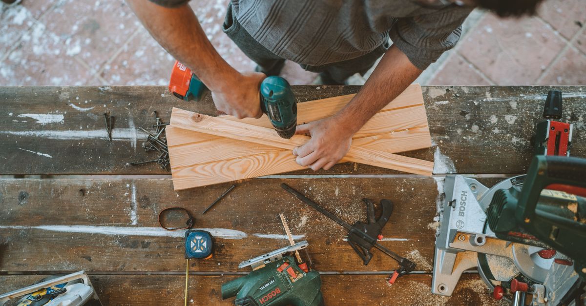 Craftsman busy drilling wooden planks in a carpentry workshop with various tools around.