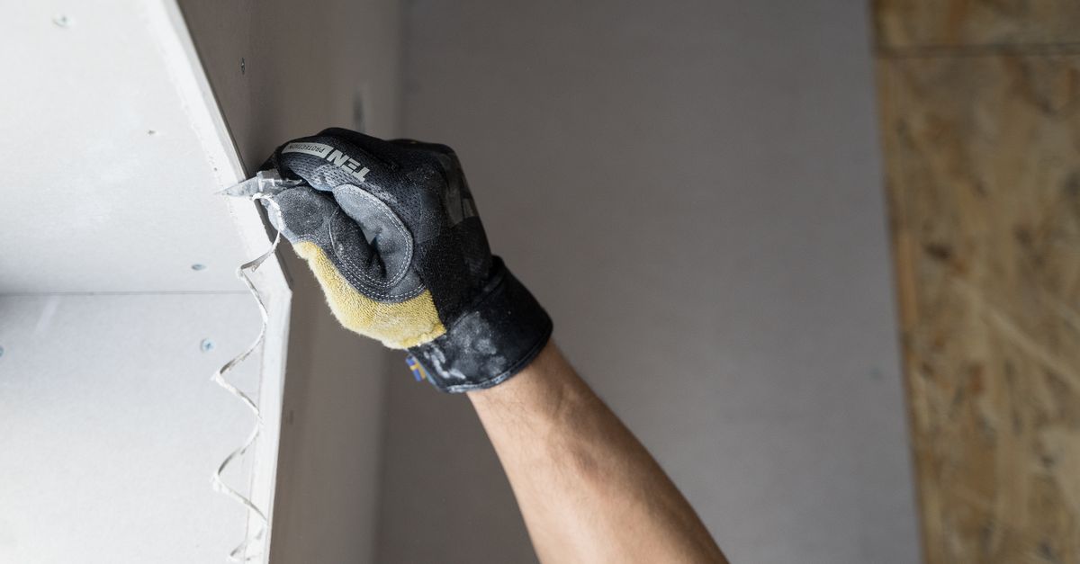 Close-up of a gloved hand applying plaster to a wall indoors in Falun, Sweden.