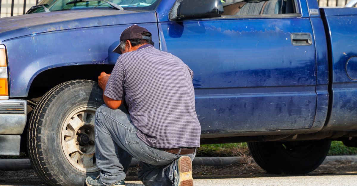 A man attentively repairing a flat tire on a blue truck in sunny Houston, Texas.