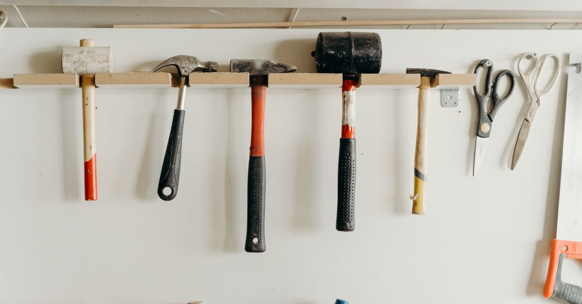 Neatly organized tools hanging on a workshop wall, including hammers and scissors.