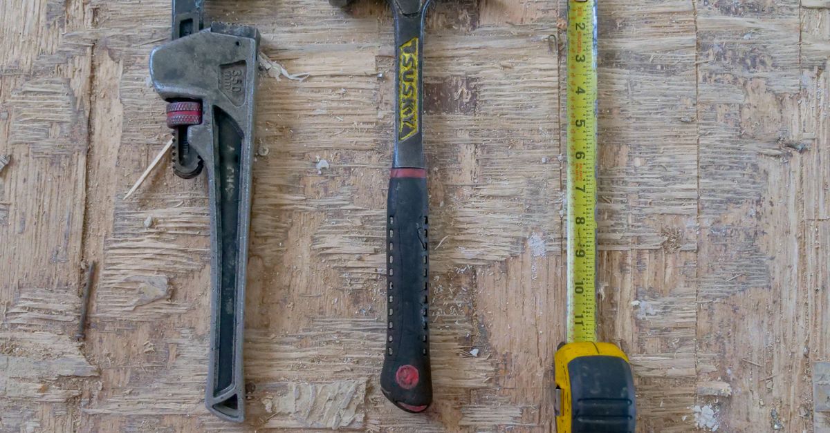 Close-up of hammer, wrench, and measuring tape on wooden surface for construction use.