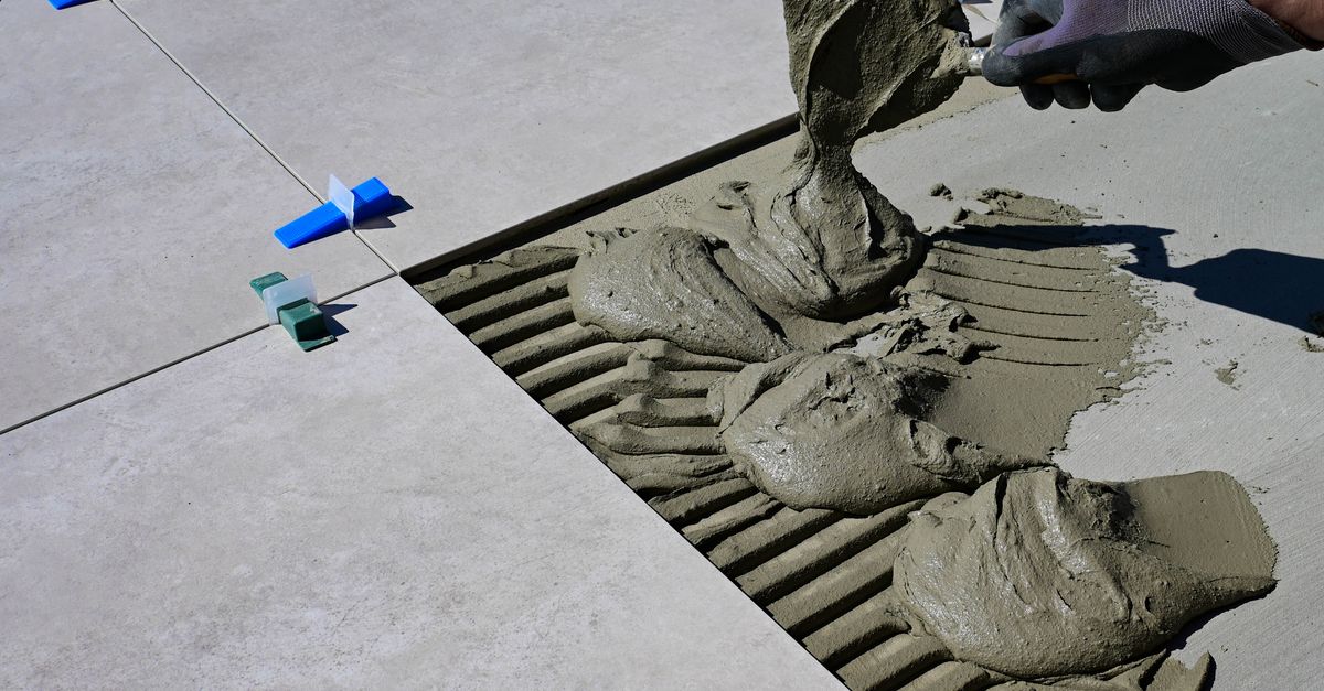 Close-up of a gloved hand applying mortar for ceramic tile installation outdoors.