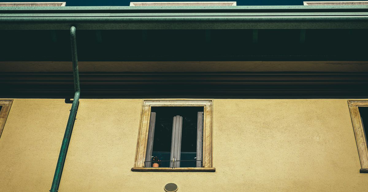 From below of aged dwelling building exterior with window on front wall in city in sunlight