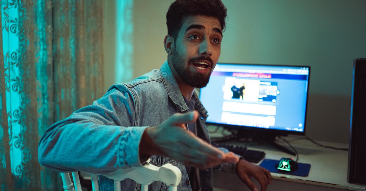 Confident young man gesturing during an online gaming conversation in a home setting.