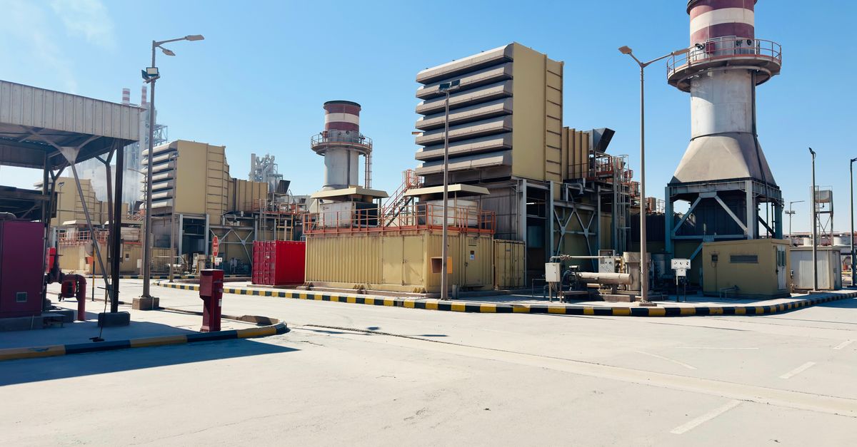 A modern power plant with turbines and chimneys under a clear blue sky in Saudi Arabia.