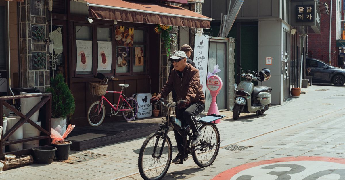 Street scene of an elderly man cycling past shops in Suwon-si, South Korea.