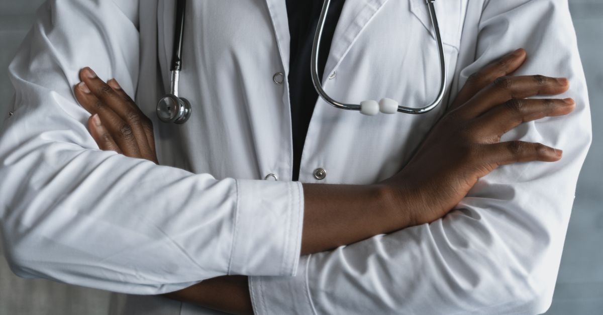 Close-up of a confident doctor in a lab coat standing with crossed arms and stethoscope.