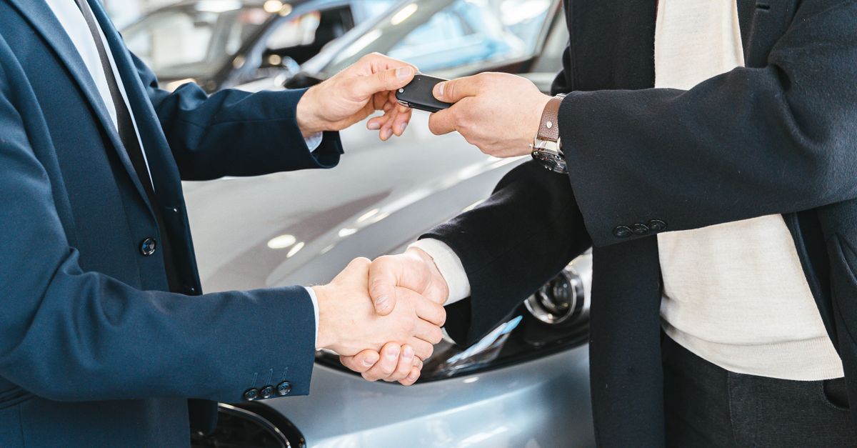 Two businessmen shaking hands and exchanging car keys in a dealership. Symbolizes a successful deal.