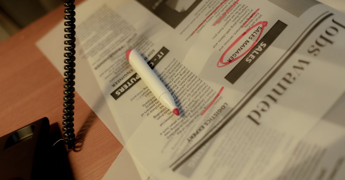 Close-up of a newspaper job section with a red marker and corded phone on a table.
