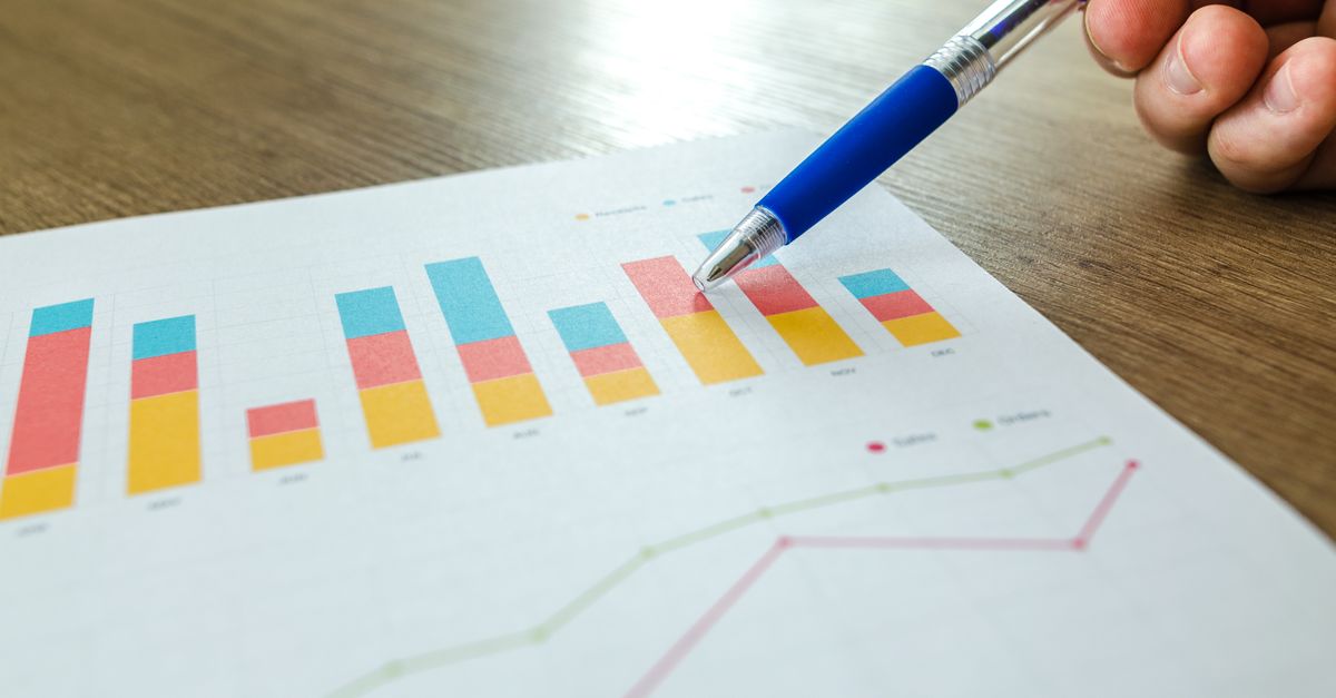 Detailed close-up of a hand pointing at colorful charts with a blue pen on wooden surface.