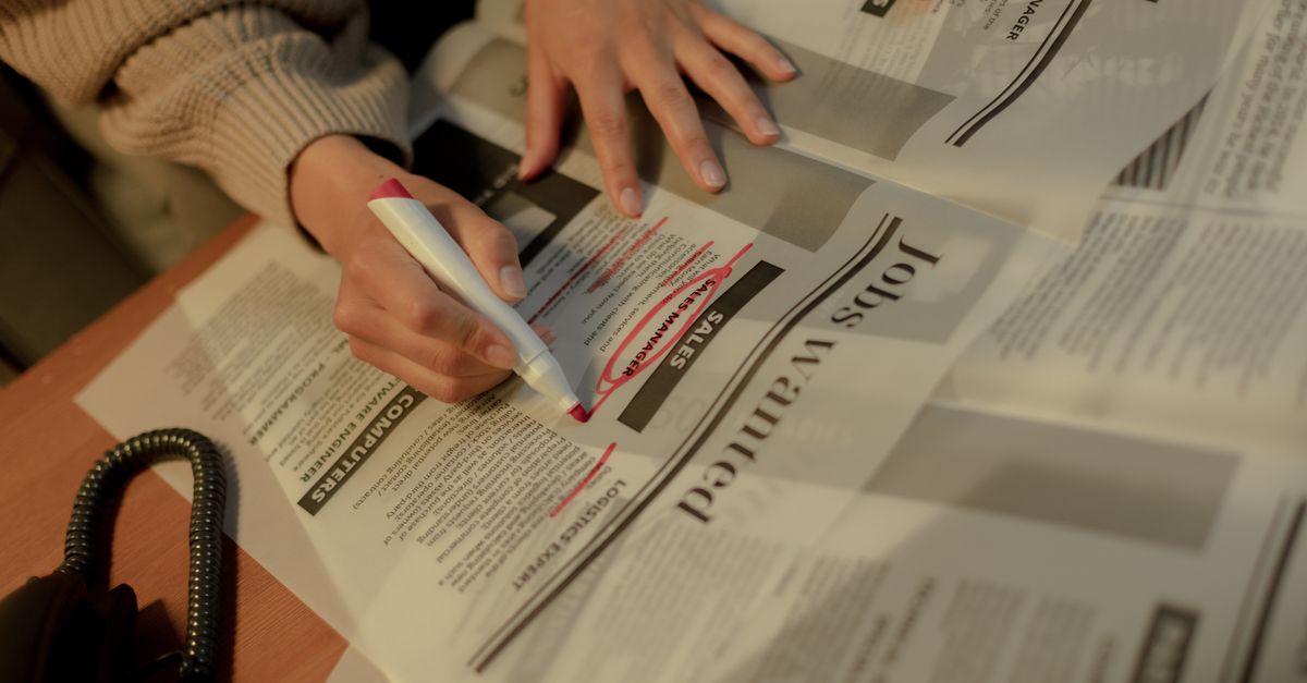 An adult woman highlights job ads in a newspaper, focusing on employment opportunities.
