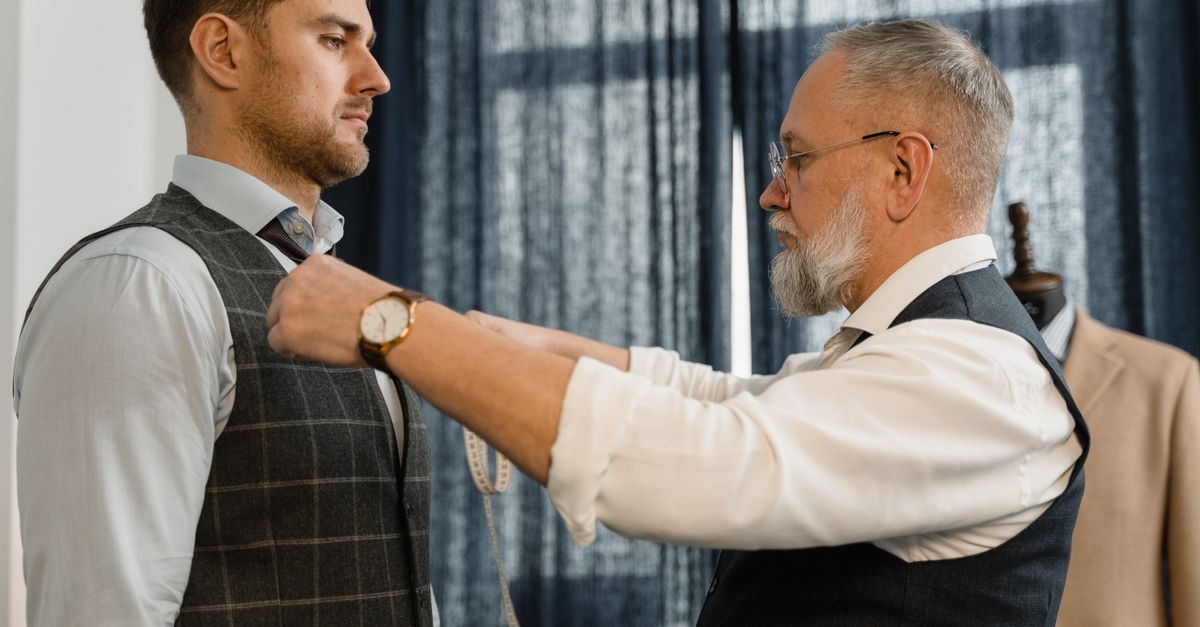 Professional tailor measuring a client for a custom suit in a workshop setting.