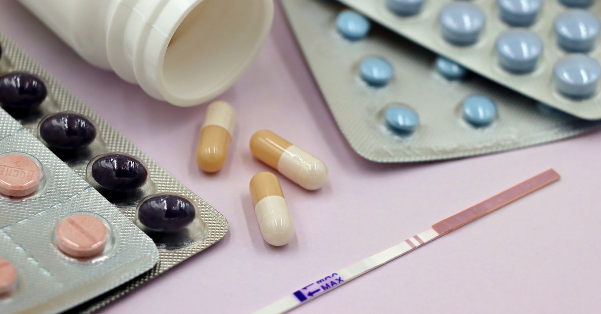 Image featuring a pregnancy test strip surrounded by various pills and capsules on a pastel background.