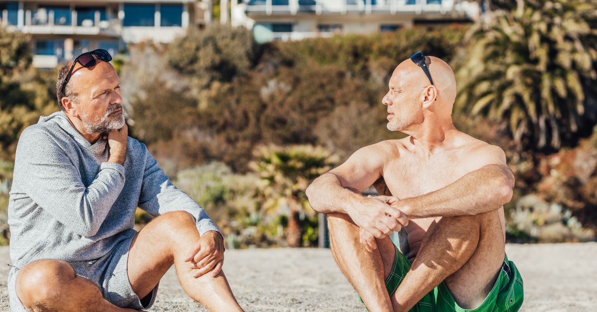 Two older men enjoy a thoughtful conversation while sitting on a sunny beach.