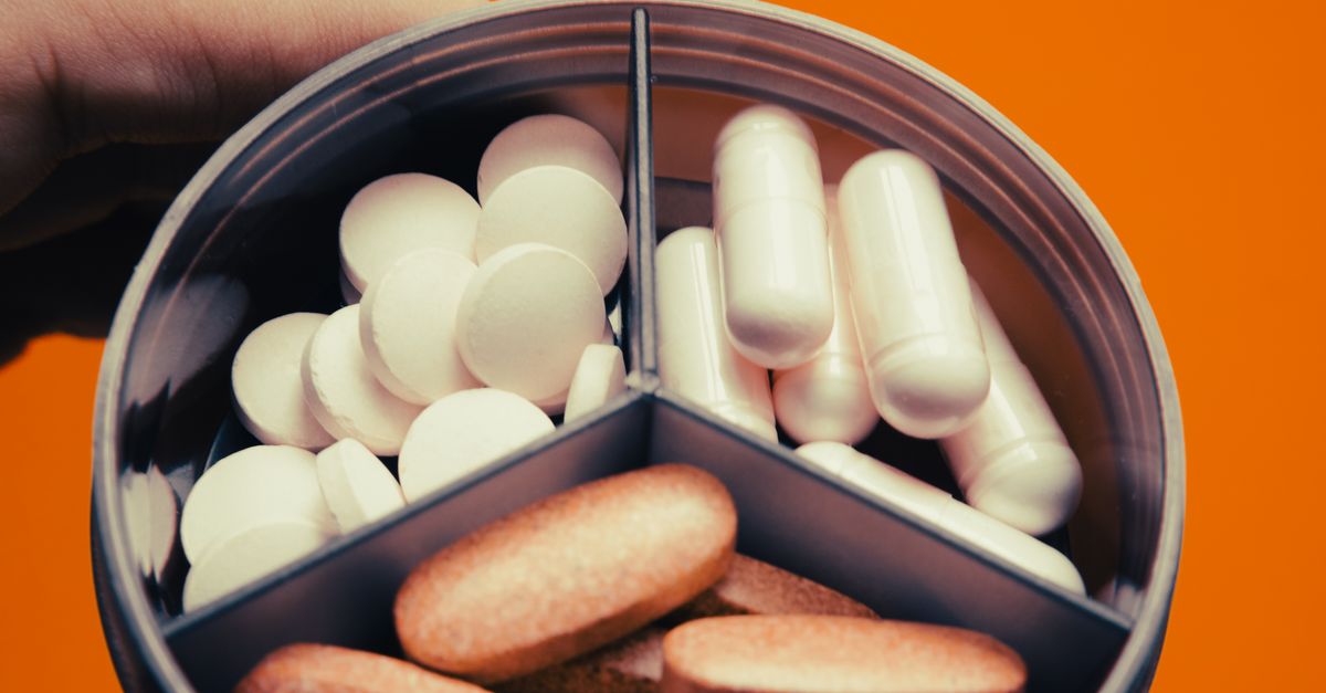 Close-up of a pill organizer containing various tablets and capsules on an orange background.