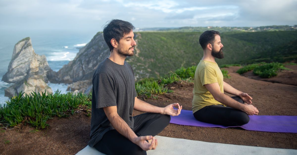 Two men practicing meditation on yoga mats overlooking a scenic cliff in Portugal.
