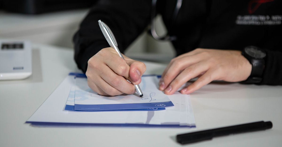A doctor writing a prescription on paper with a ballpoint pen in a clinic setting.