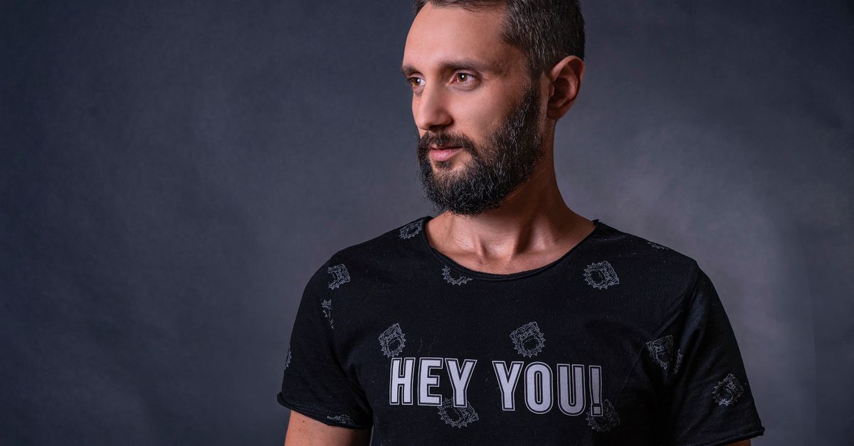 Adult man with graying hair and beard in a studio setting, wearing a 'Hey You!' t-shirt.