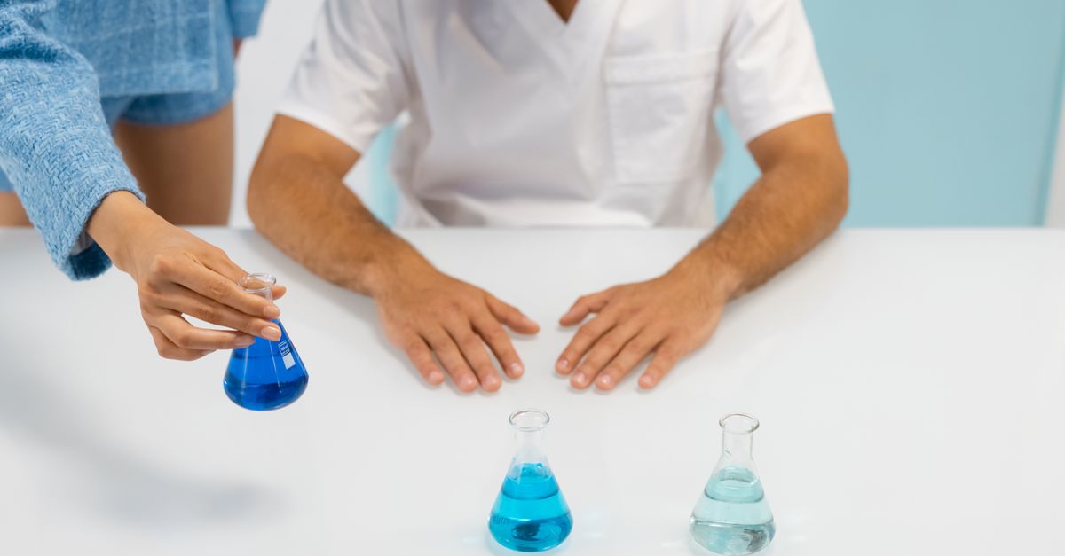 Hands conducting a laboratory experiment using Erlenmeyer flasks with blue liquid.