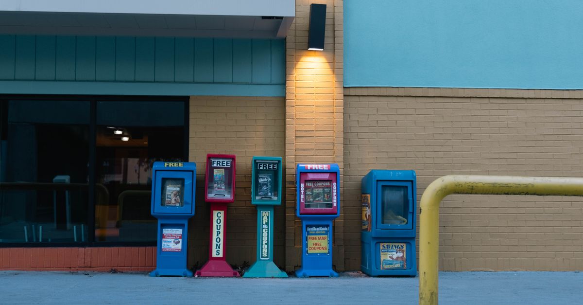 Row of colorful newspaper stands against a brick wall in urban setting during daytime.