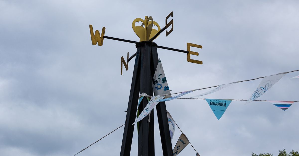 A weather vane adorned with festive bunting against a cloudy sky in Bramley, England.