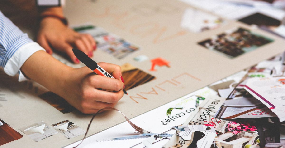 Close-up of a person writing and crafting at a cluttered desk workspace.