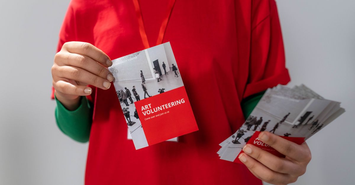 Close-up of a volunteer holding art volunteering flyers highlighting community service.