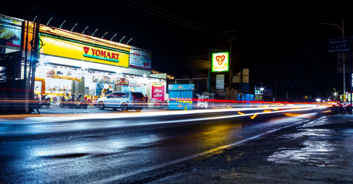 A lively city street scene in West Java showcasing long exposure light trails and a shopping mart at night.