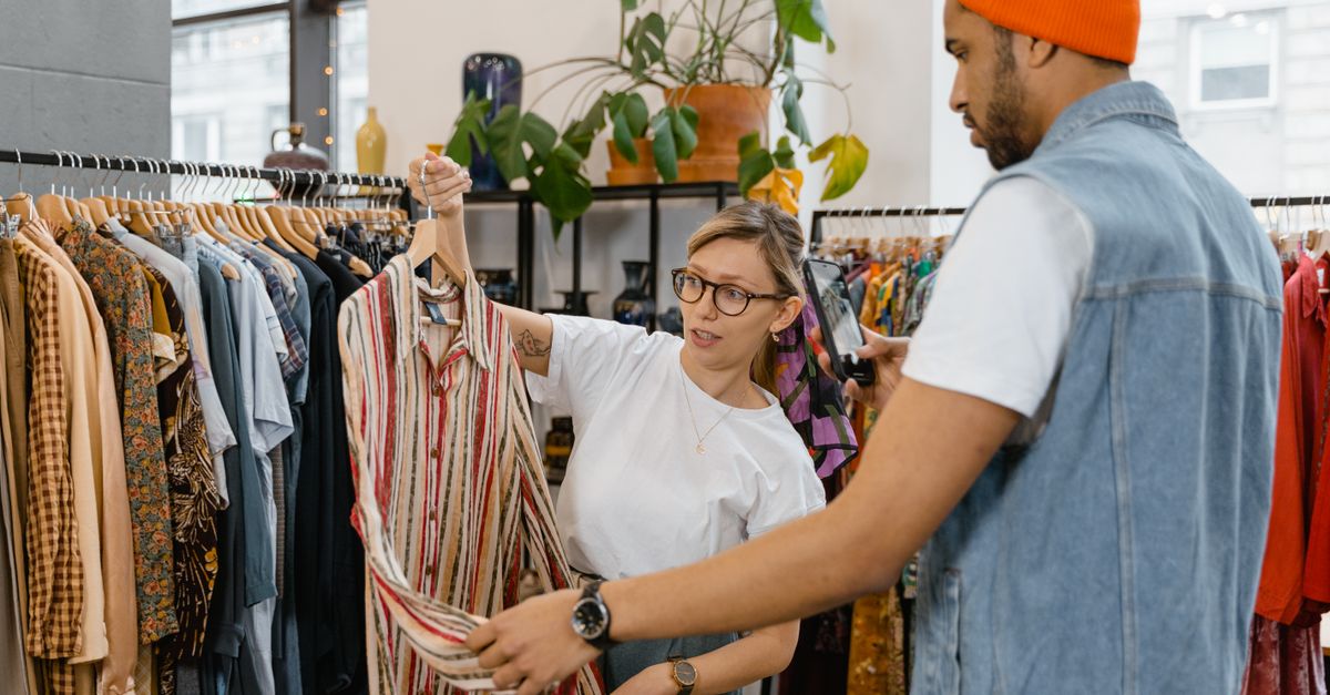 A woman helps a man choose a shirt in a modern clothing store.