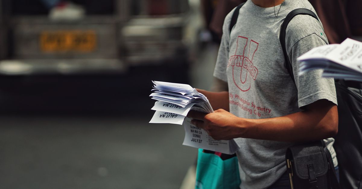 Person in casual attire distributing flyers on a busy street corner, showcasing urban life.