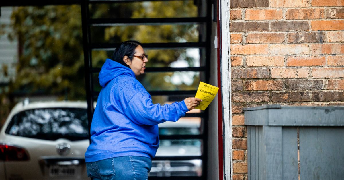 A woman in a blue hoodie delivers flyers to a brick building in a city setting.