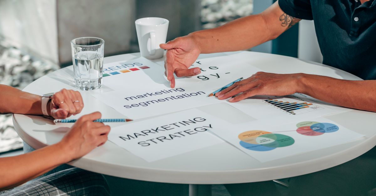 Two adults in an office discussing marketing strategy around a round table.