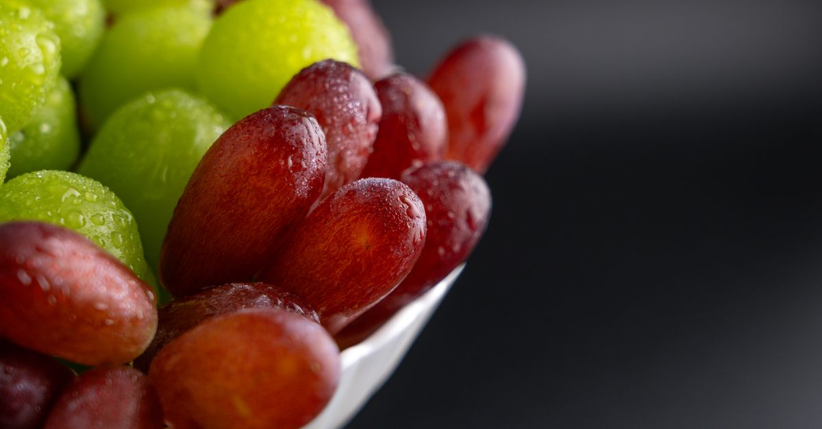 A detailed close-up of fresh red and green grapes with water droplets on a dark background.