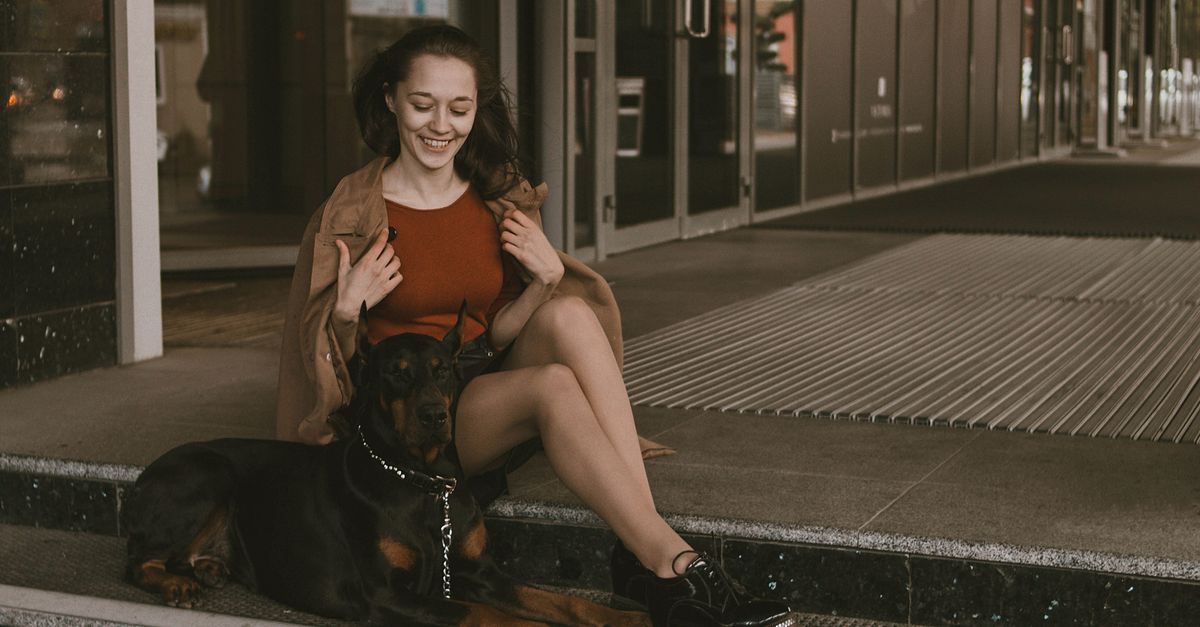 Happy woman sitting on steps with a Dobermann dog. Urban outdoor scene.