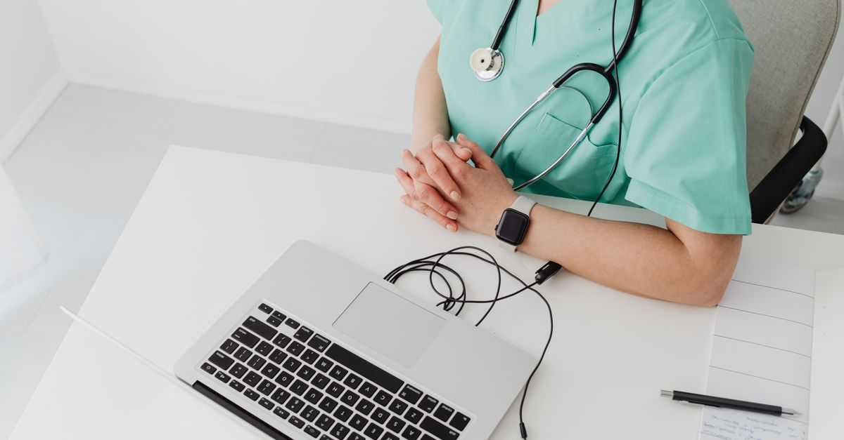 Doctor in scrubs with stethoscope conducting online consultation using a laptop.
