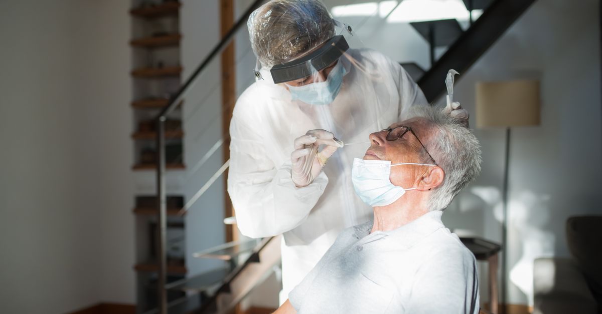 Doctor performs a COVID-19 test with protective gear on a senior man indoors.