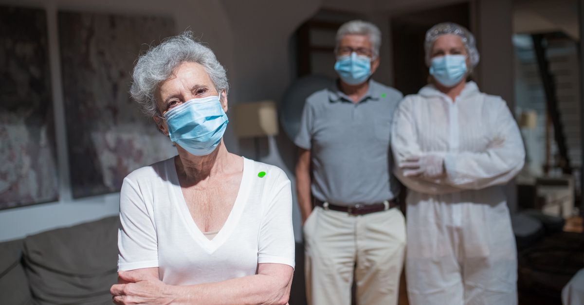Healthcare workers in protective gear assisting elderly people indoors, highlighting COVID-19 care.