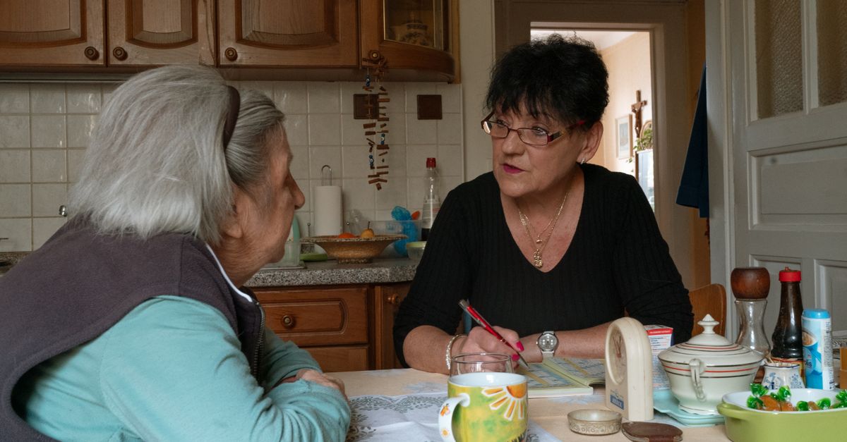 Senior woman and caregiver having a conversation in a cozy Prague kitchen setting.