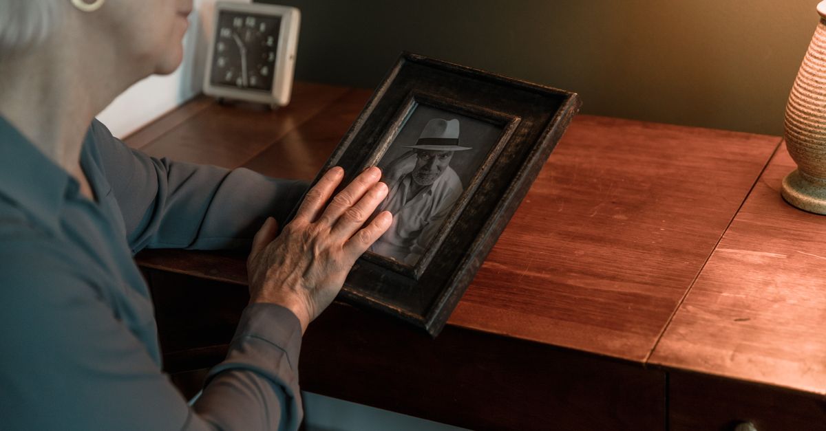 Senior woman nostalgically holding a framed photo, reflecting on memories.