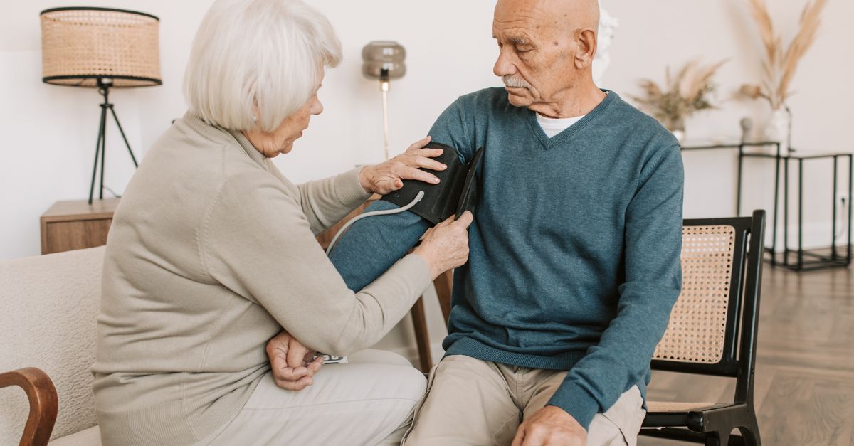 Elderly couple involved in a home blood pressure checkup, emphasizing health and care.
