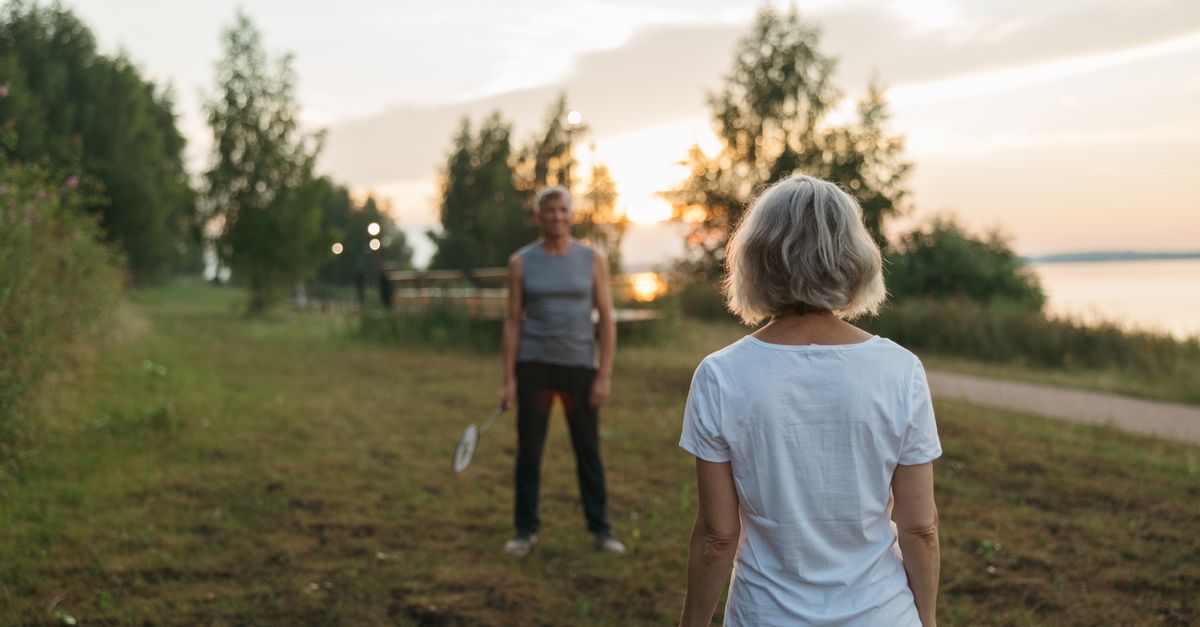 Elderly couple playing badminton outdoors at sunset, enjoying leisure time together.