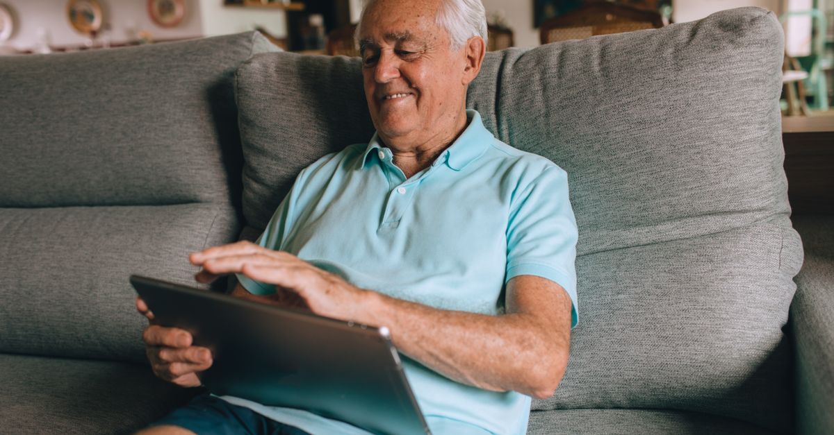 Senior man relaxing on a sofa using a tablet, enjoying technology at home.
