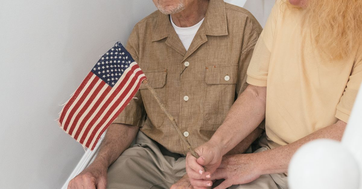 Senior couple sitting on steps indoors, holding a small United States flag together.